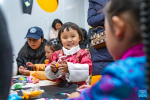 Children make necklaces with plasticine during a party at a bookstore in Lhasa, southwest China`s Xizang Autonomous Region, Feb. 3, 2024.  A unique party was held on Saturday at a bookstore for children in Lhasa City where teachers introduced the traditional customs of the Tibetan New Year. During the event, children wearing traditional Tibetan costumes enjoyed musical performance, puppet show and handicraft making, as well as a feast of `gutu`, a traditional soup dish made of flour. (Photo by Tenzin Nyida/Xinhua)
